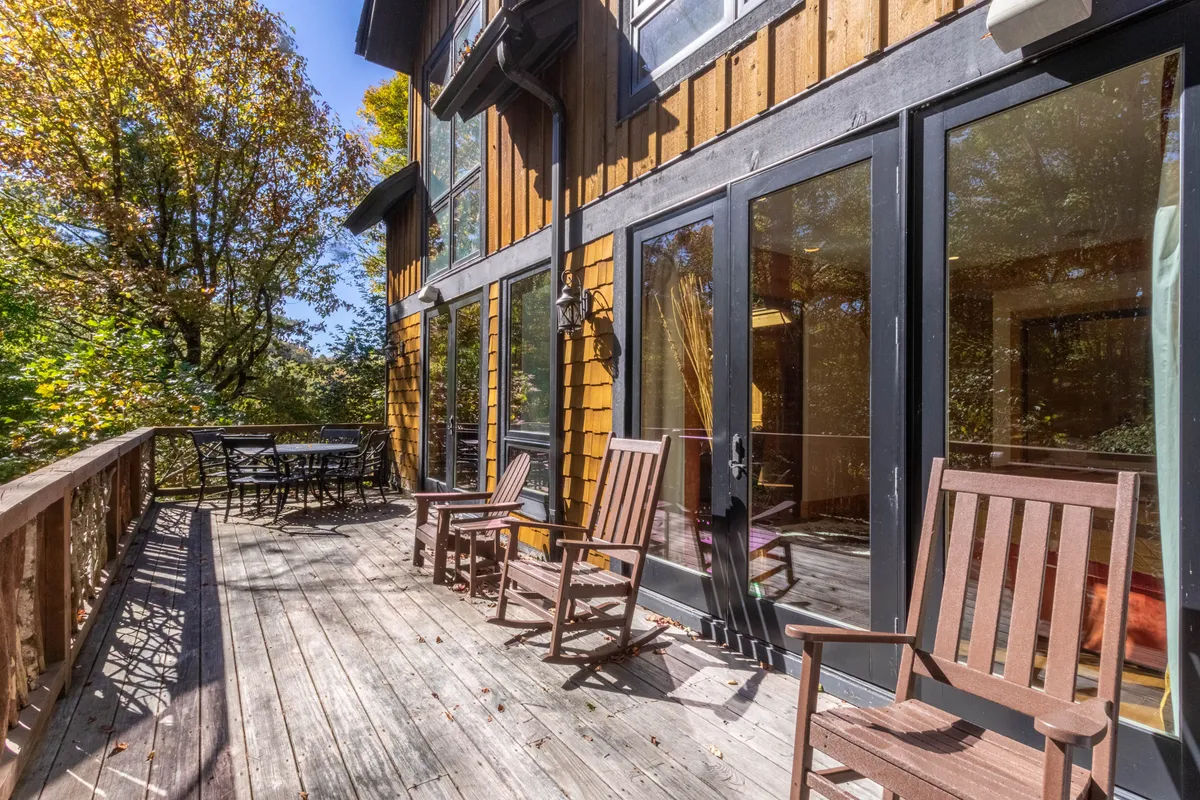 A spacious deck area bordered by trees, featuring a seating area and glass doors leading inside. The space suggests a seamless connection between indoor comfort and outdoor leisure, ideal for group gatherings or enjoying nature.