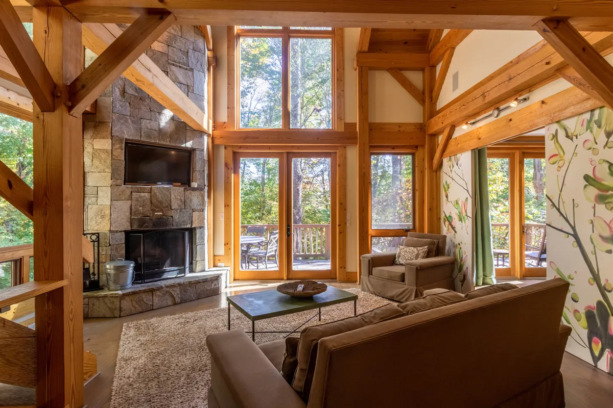 A spacious, inviting living area featuring a stone fireplace, large windows with sunset views, comfortable seating, and artistic floral décor. The layout is open and encourages group conversation or relaxation while enjoying the natural surroundings.