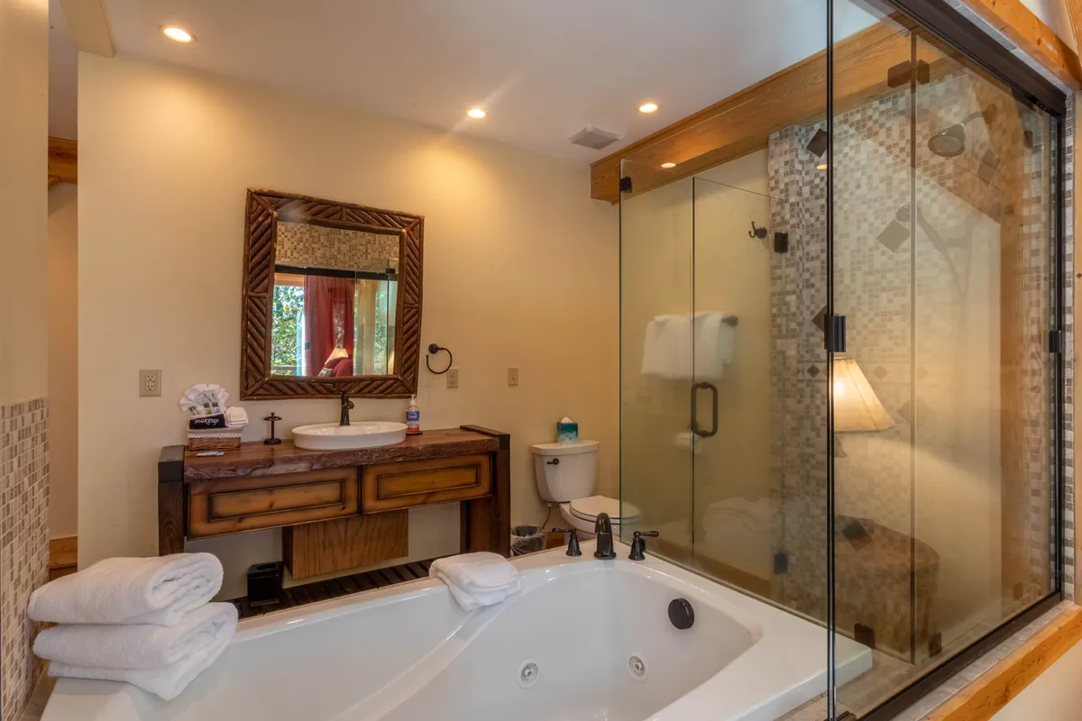 An ensuite bathroom with a tranquil mood, featuring a jacuzzi tub, a stylish wooden vanity with a mirror, and a glass shower enclosure. The space exudes modern comfort and provides the ultimate place to unwind after a day of exploration.