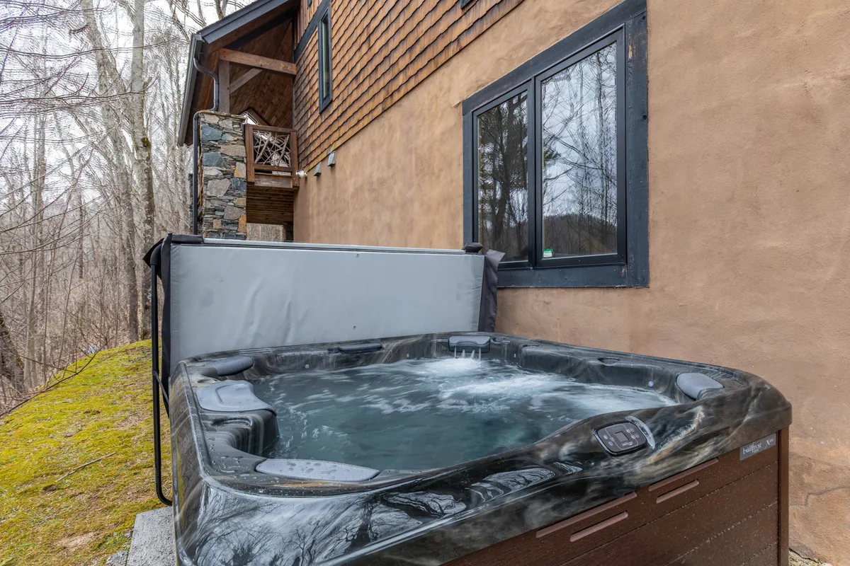 A serene exterior view depicting a hot tub set on a wooden deck surrounded by tall trees. Guests relax in the hot tub, chatting and soaking in the tranquility of nature after a day of resort activities.
