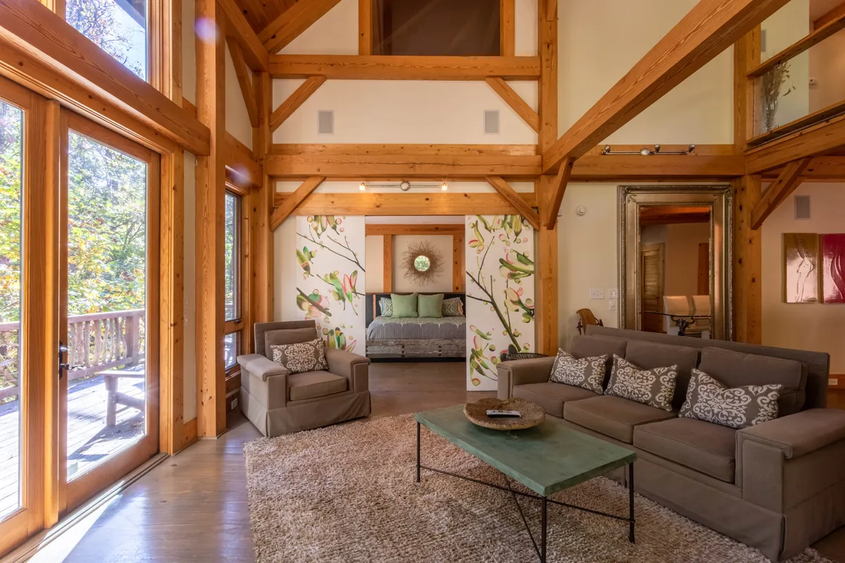 A welcoming living area with large glass doors opening onto a deck, comfortable seating, and decorative touches. The space is bathed in natural light and offers a seamless transition to the outdoors, inviting guests to enjoy both indoor relaxation and outdoor exploration. The view through the doors hints at the landscapes and activities awaiting just steps away.
