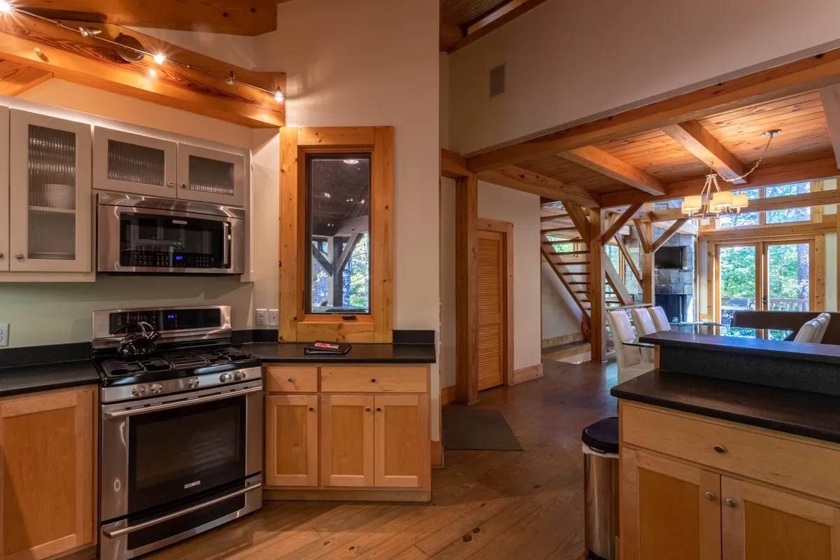 A modern kitchen with wooden cabinetry, state-of-the-art appliances, and a large window that brings in plenty of natural light. The space is clearly designed for hosting group meals and culinary experiences.