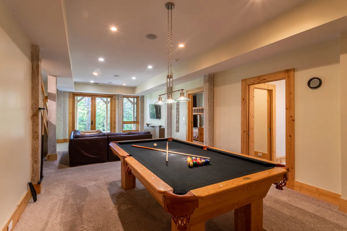 A spacious entertainment room featuring a pool table, a cozy sofa, and large windows that fill the space with natural light. The windows offer a glimpse of the outdoors, suggesting easy access to recreation beyond the walls. The casual setup encourages friendly competition and relaxed afternoons inside when the weather doesn't permit outdoor activities.